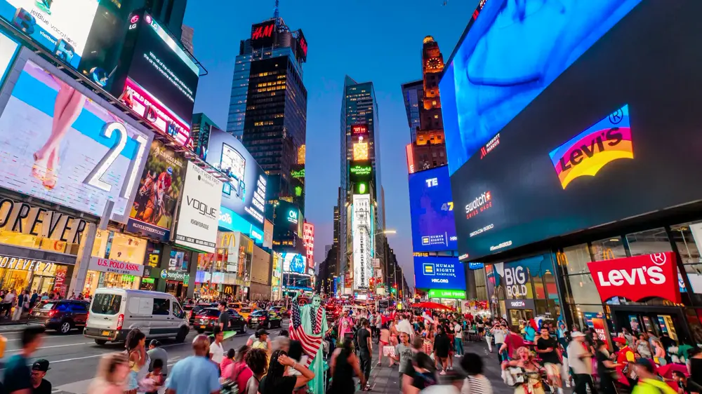 La place Times Square à New-York, lors de la tombée de la nuit, avec beaucoup de monde circulant